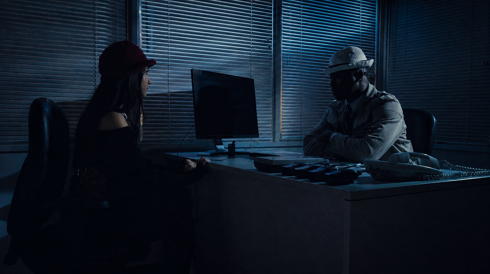 Two characters face each other across a desk in the neo-noir sequence of Five More Minutes